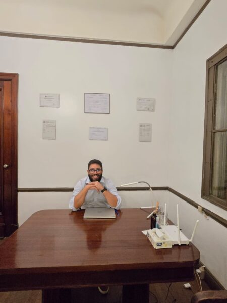 Terapeuta en el consultorio Terapeuta sentado en su silla, delante de él, el escritorio con los titulos de fondo